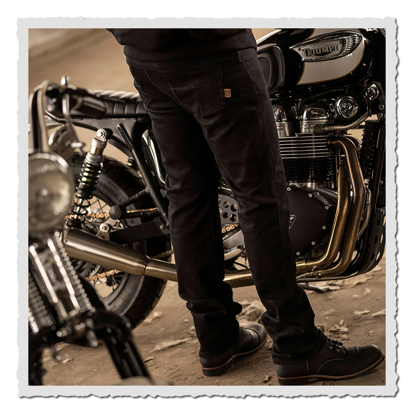 Unterkörper einer Person in schwarzer Hose vor einem klassischen Motorrad mit glänzenden Metallteilen.